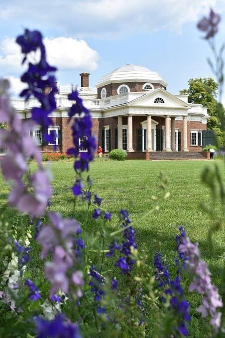This may contain: purple and white flowers are in front of a large building with columns on the roof