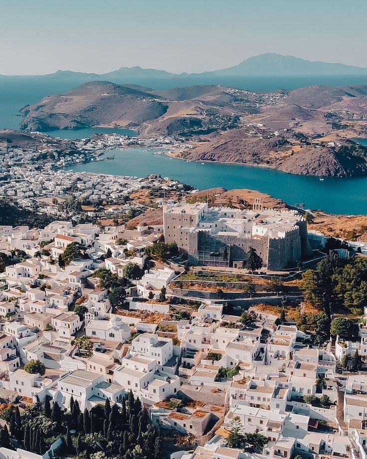 This may contain: an aerial view of a city with mountains in the background and water on the other side