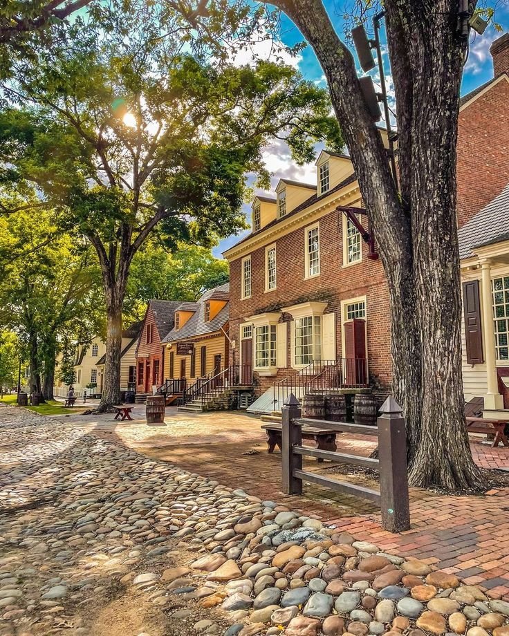 This may contain: an old brick building sitting next to a tree on a cobblestone road in front of it
