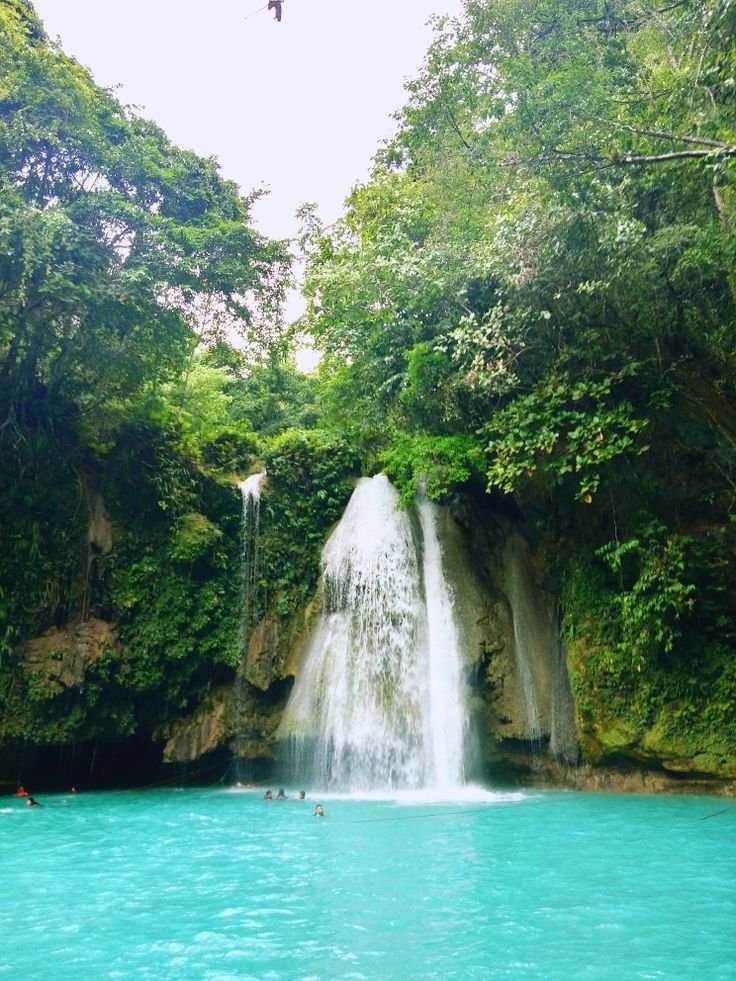 This may contain: people are swimming in the blue water near a large waterfall with a bird flying over it