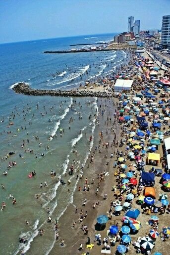 This may contain: many people are on the beach with umbrellas and in the water at this time