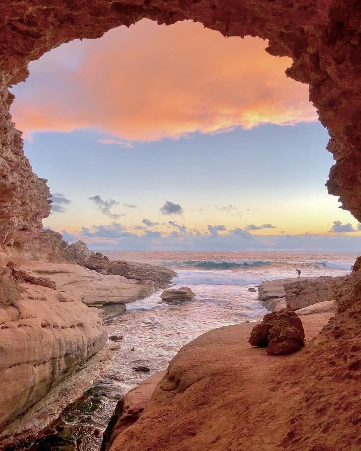 This may contain: the view from inside a cave looking out onto the ocean at sunset or dawn with pink clouds