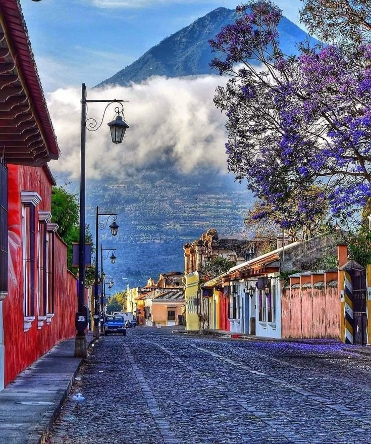 This may contain: a cobblestone street with colorful buildings and mountains in the backgrouund