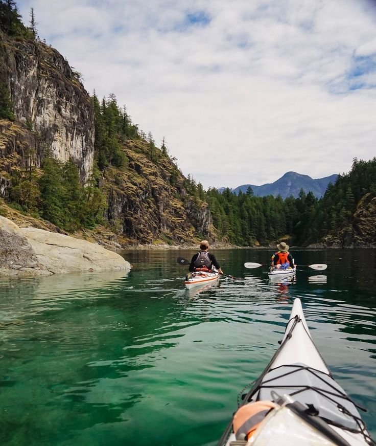 This may contain: two people are paddling their kayaks in the water near some mountains and trees