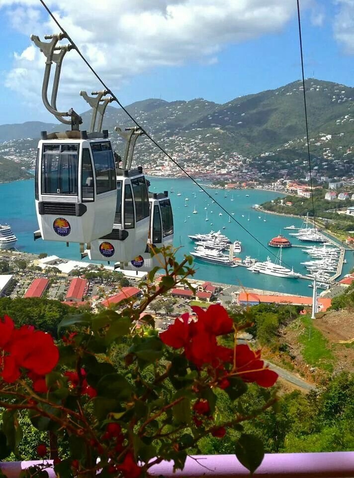 This may contain: a cable car going over the ocean with boats in the water and mountains behind it