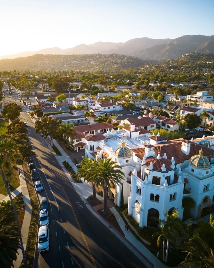 This may contain: an aerial view of a town with palm trees and mountains in the background at sunset
