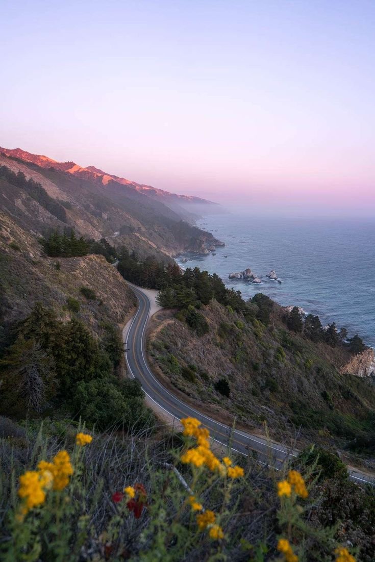 This may contain: a winding road near the ocean at sunset