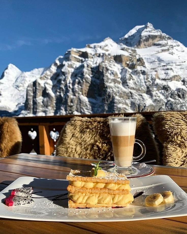 This may contain: there is a plate with food on it and a cup of coffee in front of the mountain