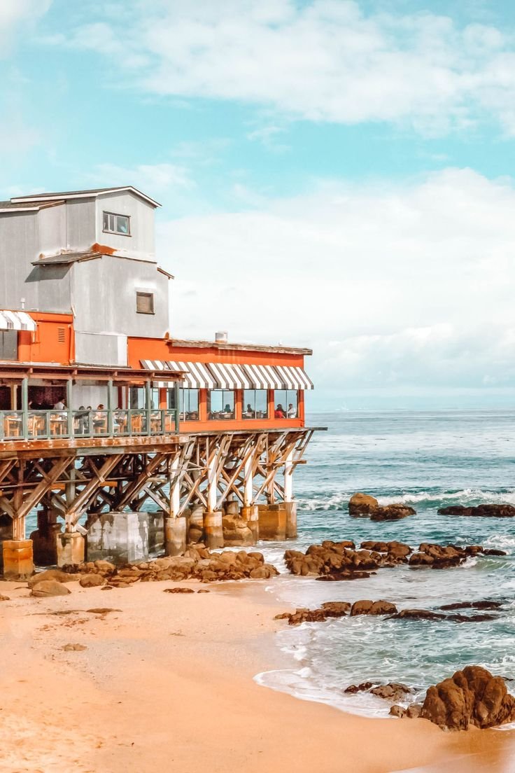 This may contain: an orange and white building sitting on top of a beach next to the ocean