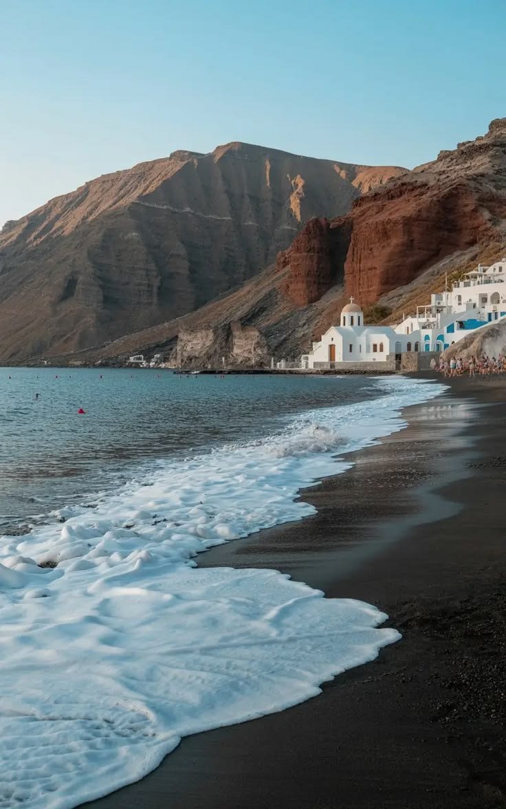 This may contain: a beach with waves coming in to shore and houses on the hill side behind it