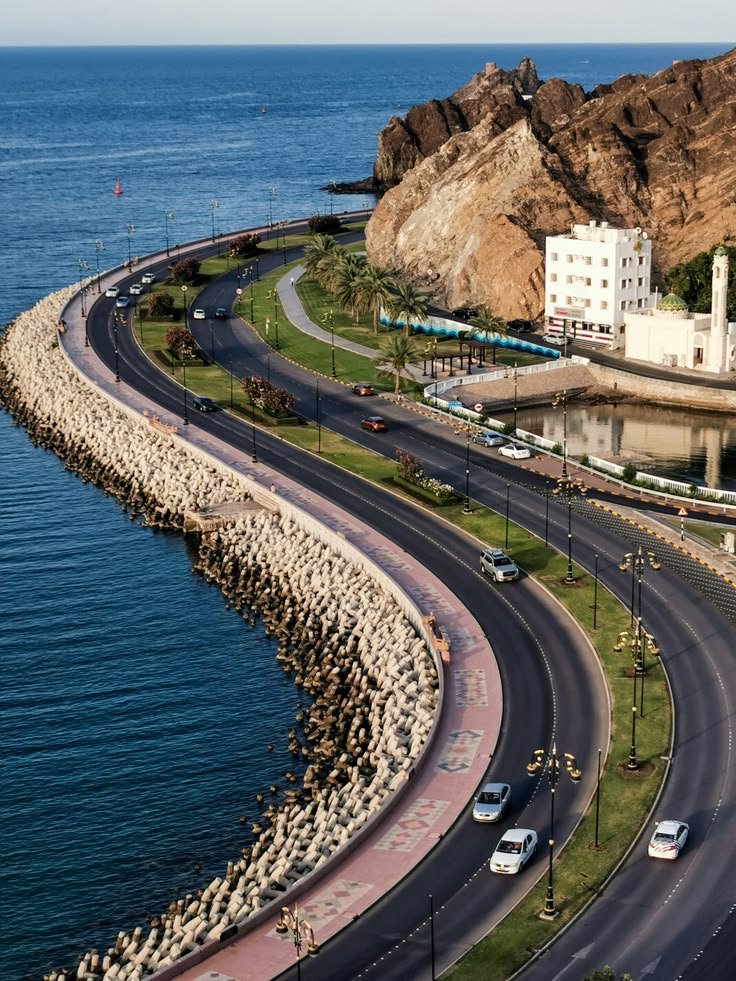 This may contain: an aerial view of a road near the ocean with cars driving on it and mountains in the background