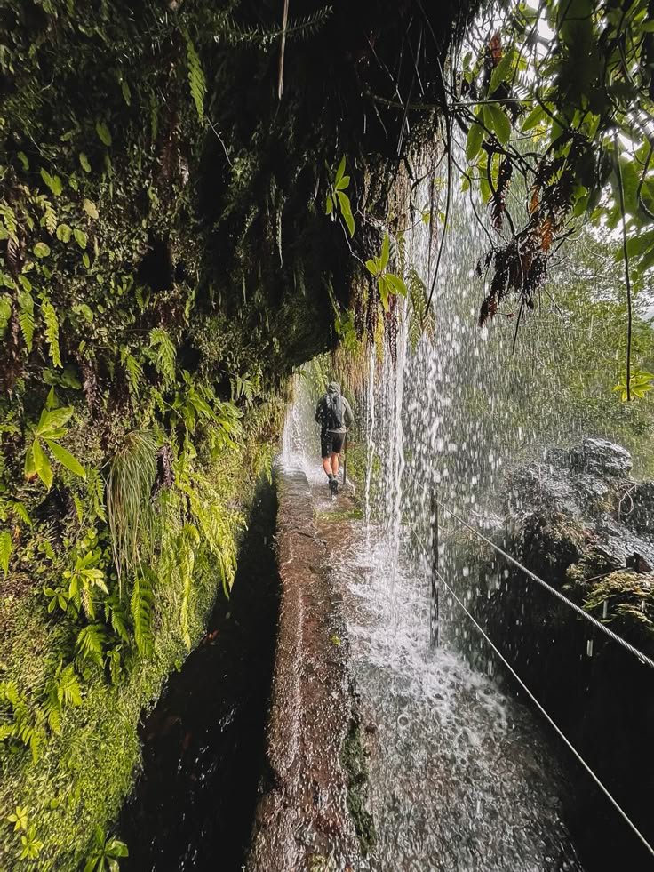 This may contain: a man walking down a path next to a waterfall