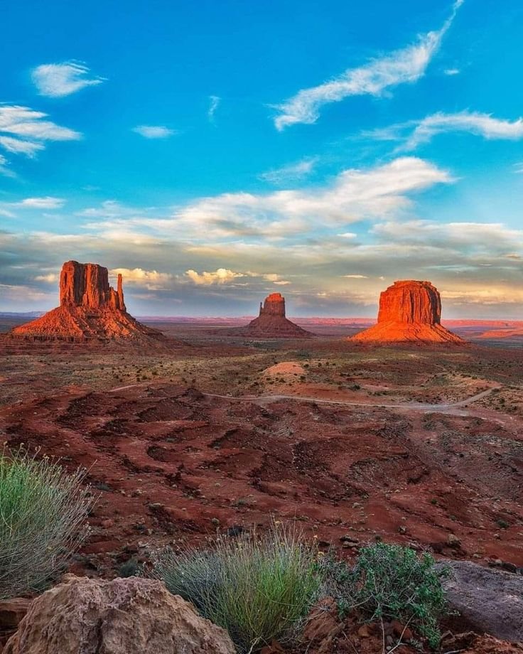 This may contain: the desert is full of red rocks and green plants, as well as clouds in the sky