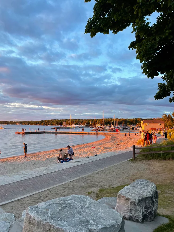 This may contain: people are on the beach at sunset with boats in the water and rocks around them