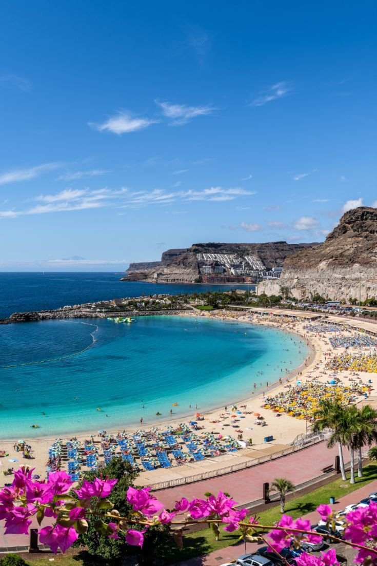 This may contain: the beach is crowded with people and umbrellas near the blue water on a sunny day