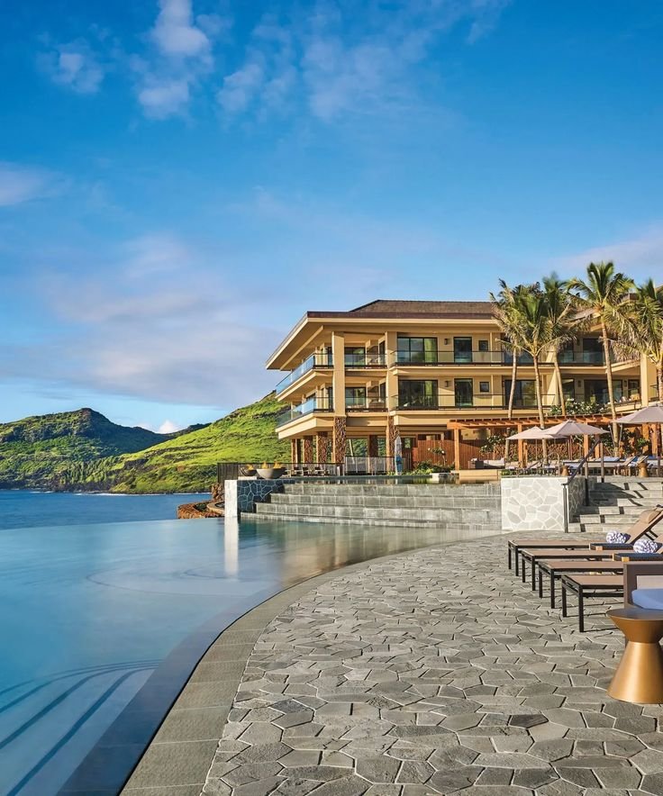 This may contain: an outdoor swimming pool with chaise lounges and umbrellas next to the ocean