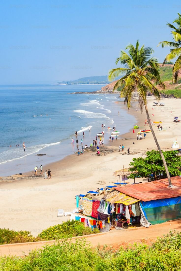 This contains: Golden sandy coastline under a bright blue sky with lush greenery in North Goa