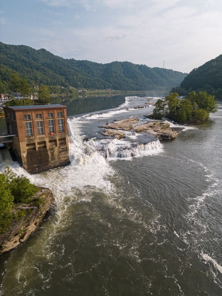 This may contain: an aerial view of a river with rapids and buildings in the distance, surrounded by mountains