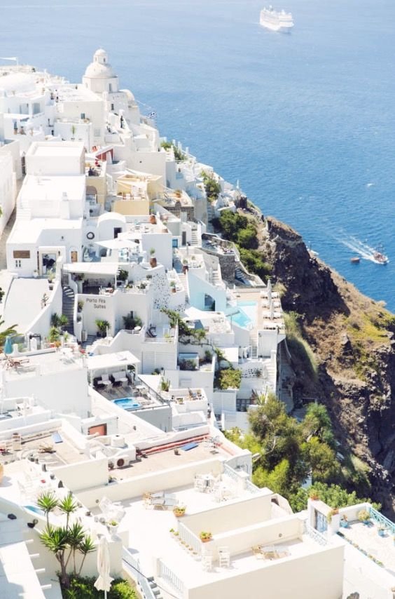 This may contain: an aerial view of white buildings on the cliff overlooking the ocean and yachts in the water