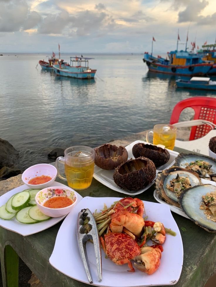 This may contain: there are many plates of food on the table next to the water with boats in the background