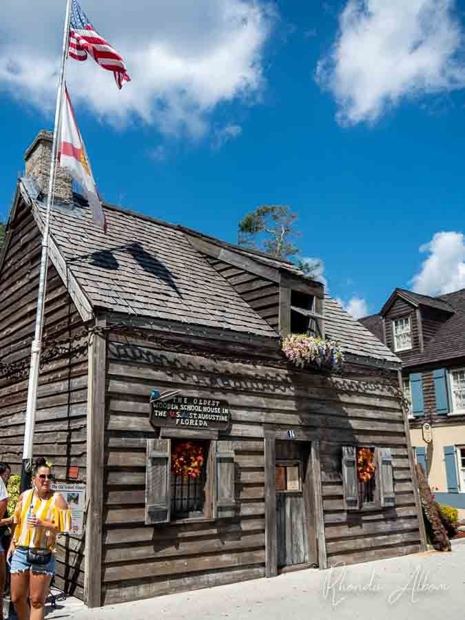 This may contain: an old log building with a flag on top and people walking around it in front