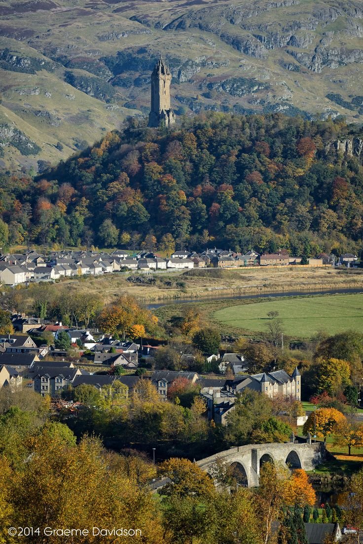 This may contain: a small town surrounded by mountains in the fall season with trees and houses on either side