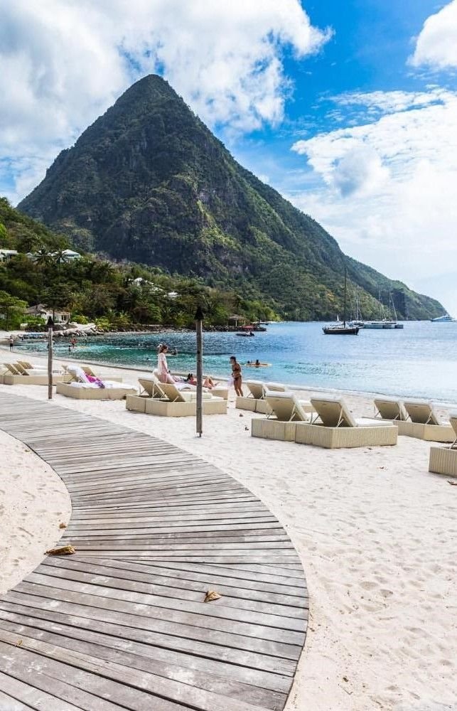 This may contain: a wooden walkway leading to the beach with chaise lounges and people on it