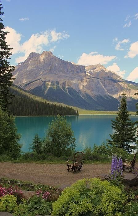 This may contain: two park benches sitting on the side of a lake with mountains in the back ground