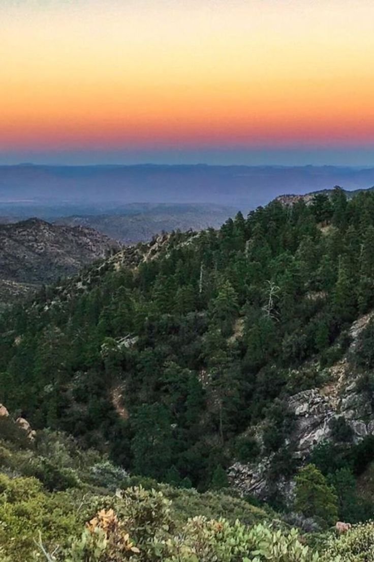 This may contain: the sun is setting in the distance on top of a mountain with trees and bushes