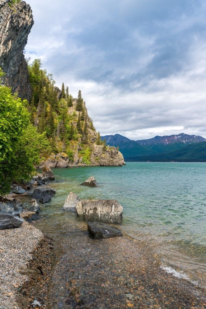 This may contain: the water is crystal blue and clear with rocks in it, along side some green trees