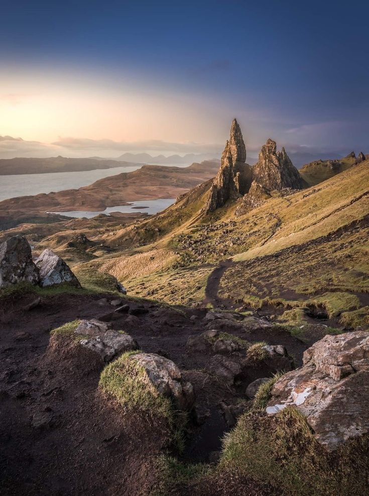 This may contain: the mountains are covered in green grass and rock formations, as the sun is setting