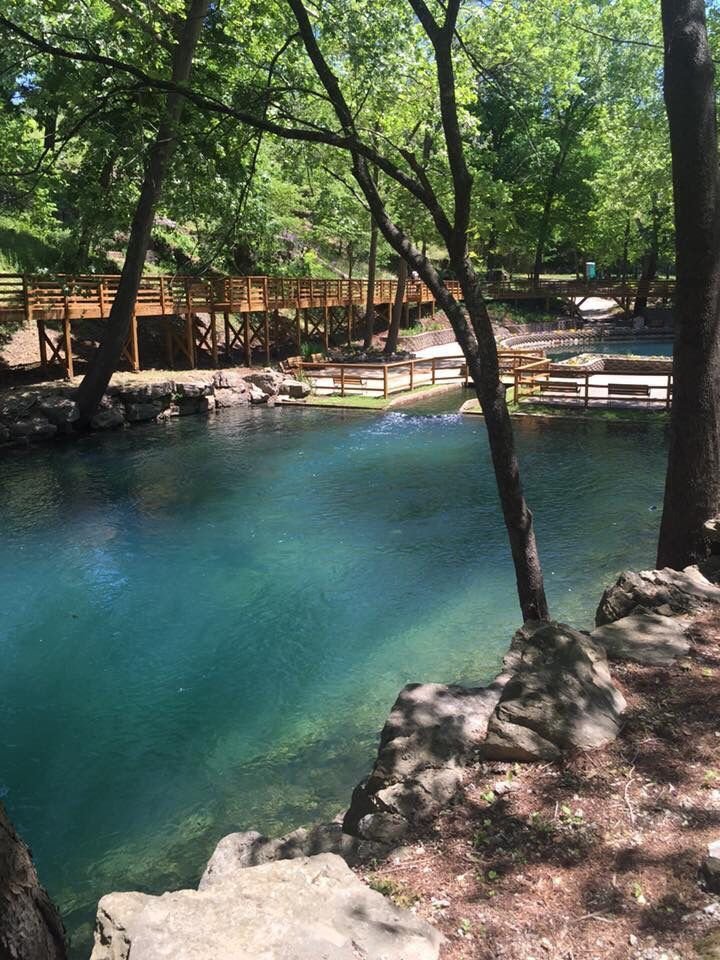 This may contain: the water is very blue and clear in this park area with trees, rocks and benches