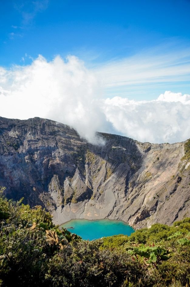 This may contain: a blue lake in the middle of a mountain range with clouds above it and trees below