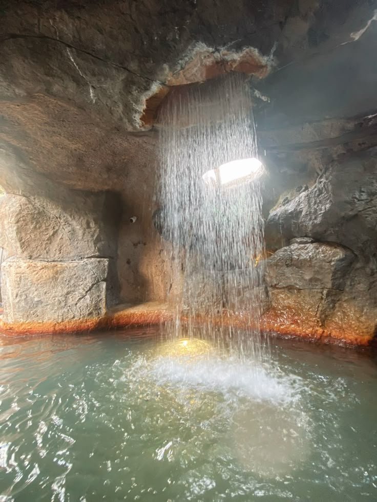 This may contain: a waterfall coming out of the side of a cave into a pool filled with water