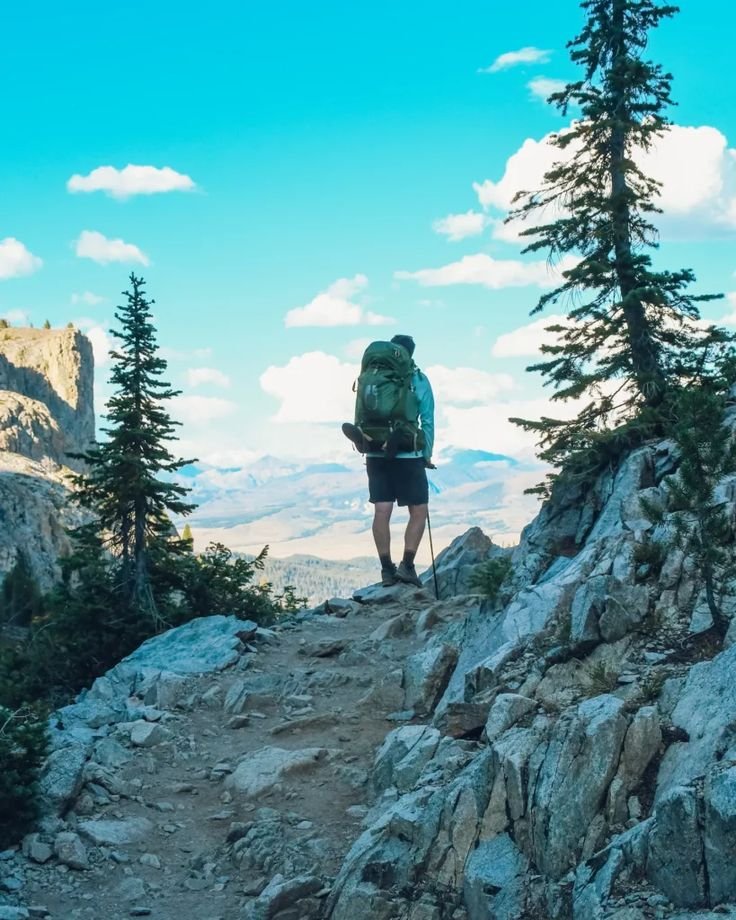 This may contain: a man with a backpack standing on top of a rocky hill looking at the mountains