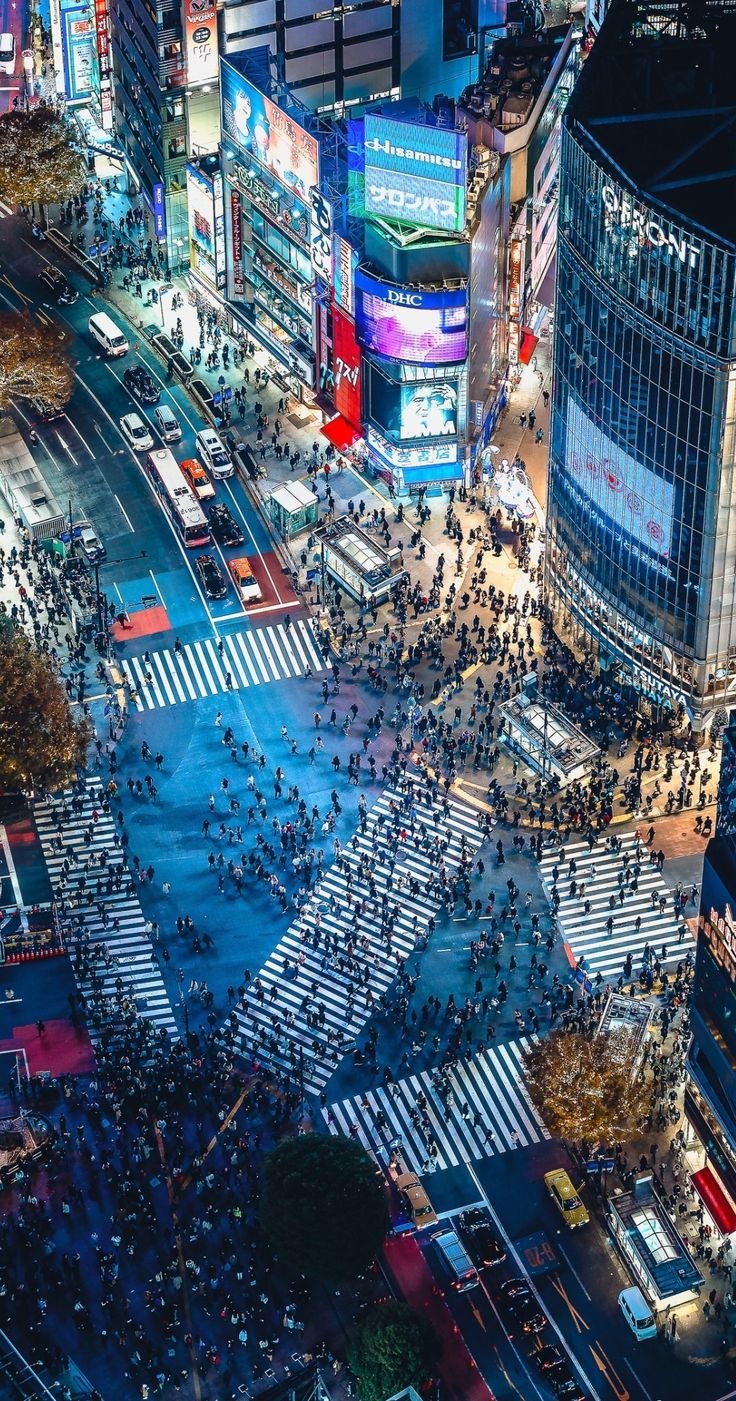 This may contain: an aerial view of a city at night with lots of lights and people crossing the street