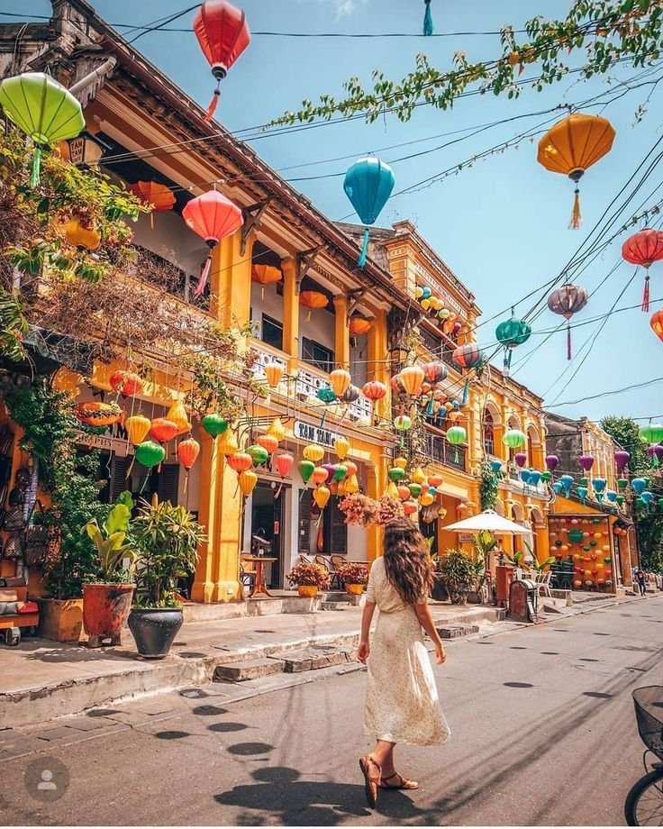 This may contain: a woman is walking down the street in front of some buildings with lanterns hanging from it