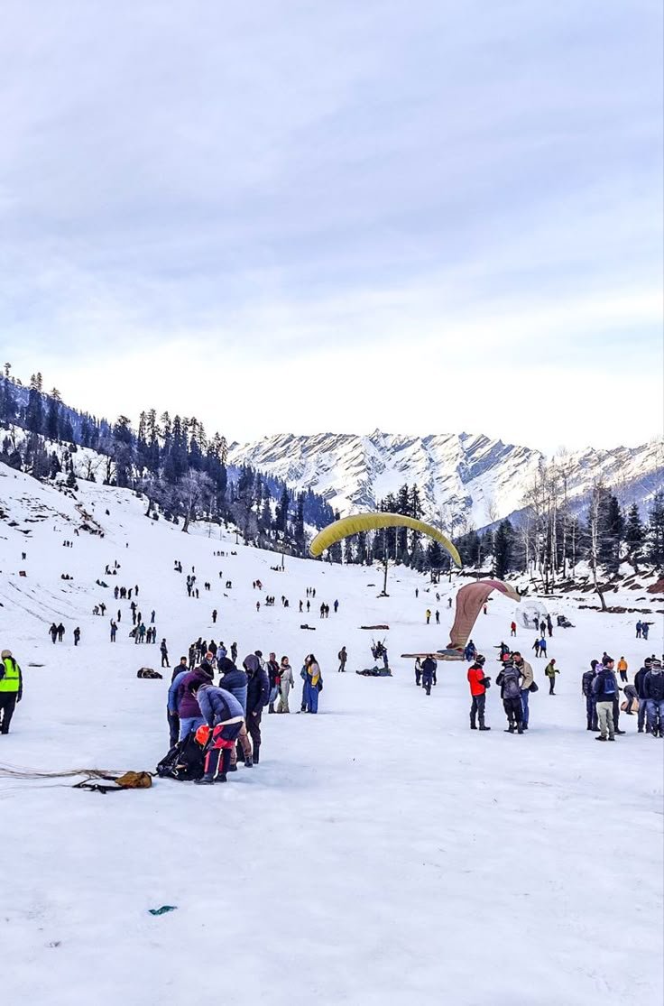 This may contain: a group of people standing on top of a snow covered slope next to a mountain