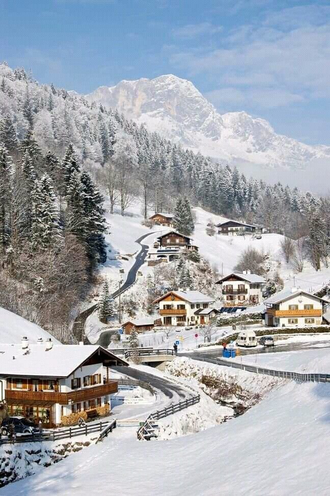This may contain: a snow covered mountain with houses on it's sides and mountains in the background