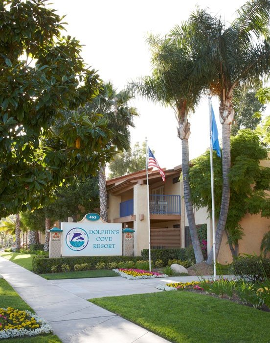 This may contain: an apartment building with landscaping and flags on the front lawn, along with palm trees