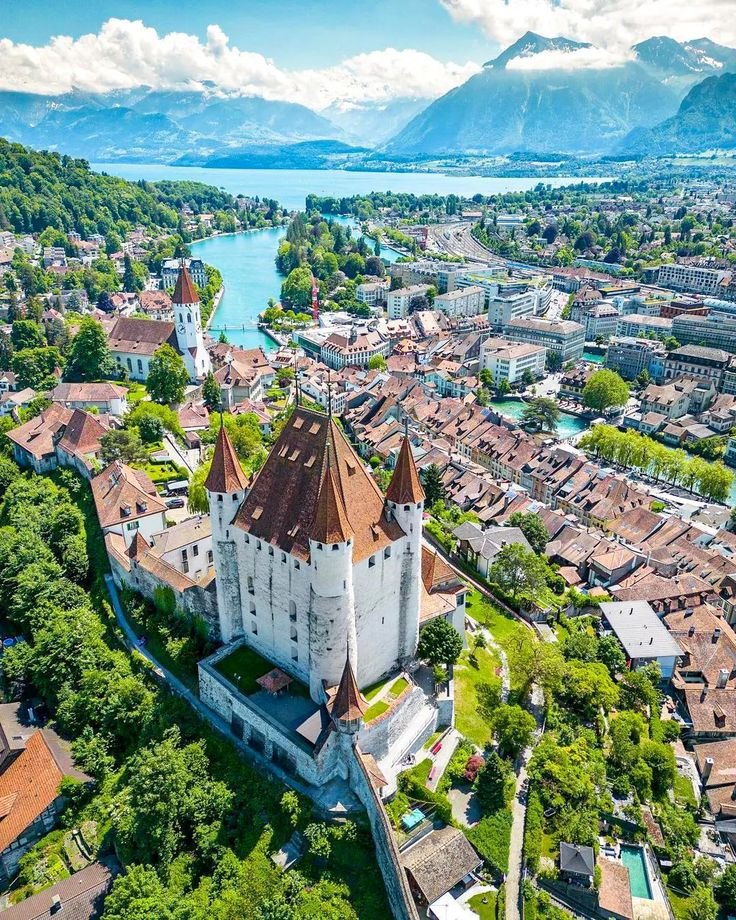 This may contain: an aerial view of a city with mountains in the background and water on the other side