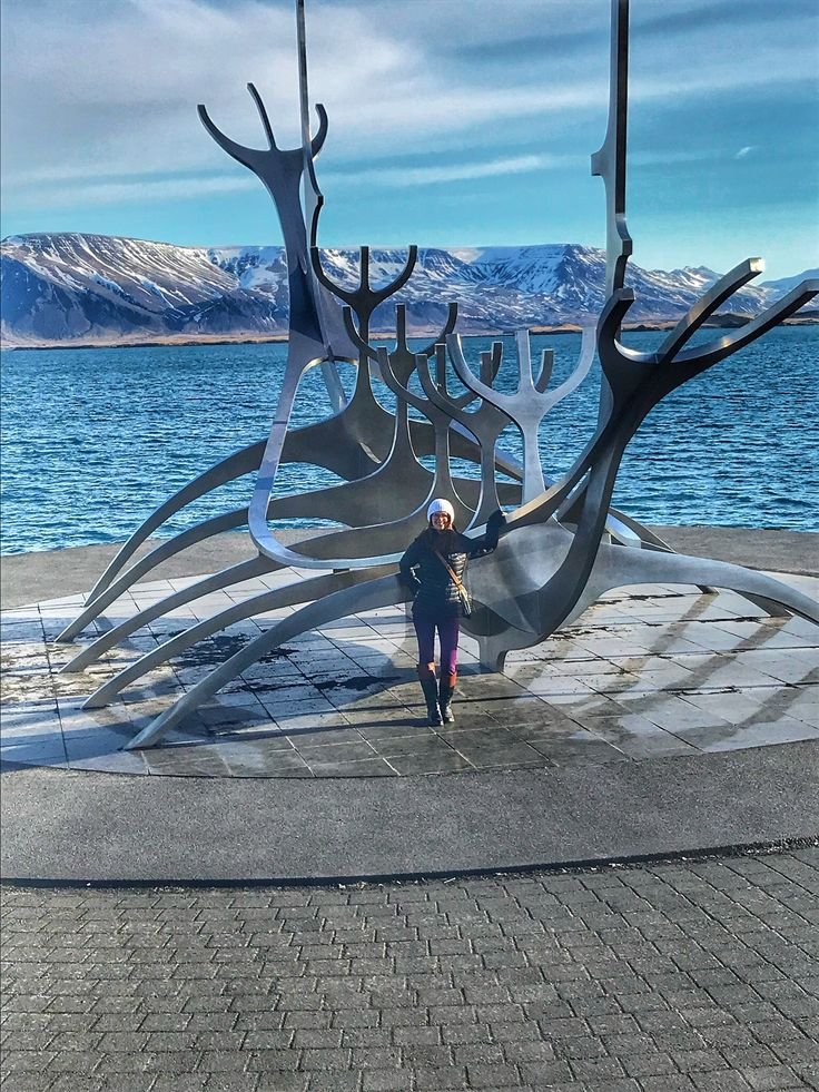 This may contain: a woman standing in front of a large metal sculpture on the side of a body of water