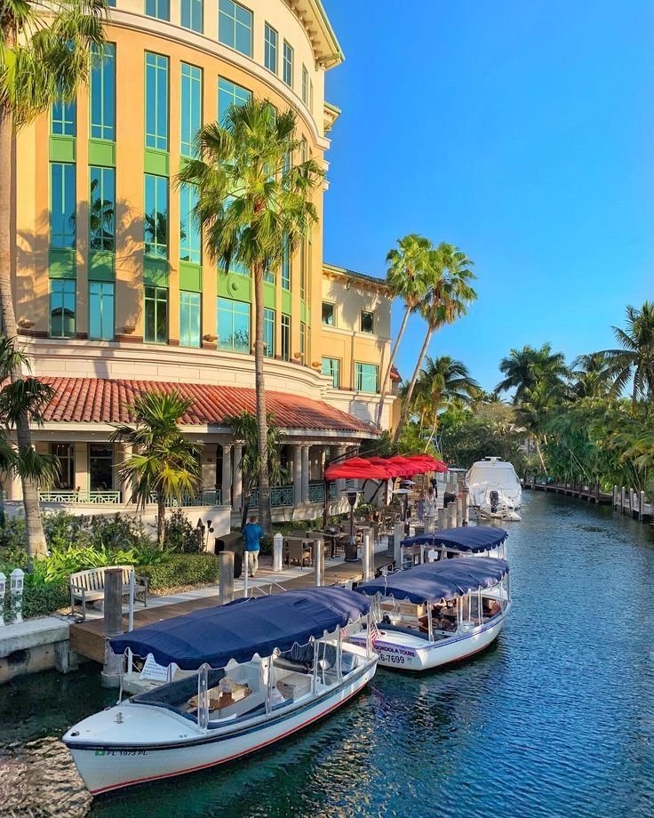 This may contain: several boats are docked in front of a building on the water with palm trees around them