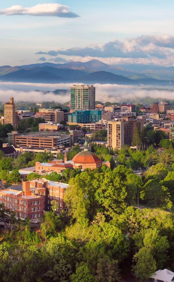 This may contain: the city is surrounded by trees and mountains with low clouds in the sky above it