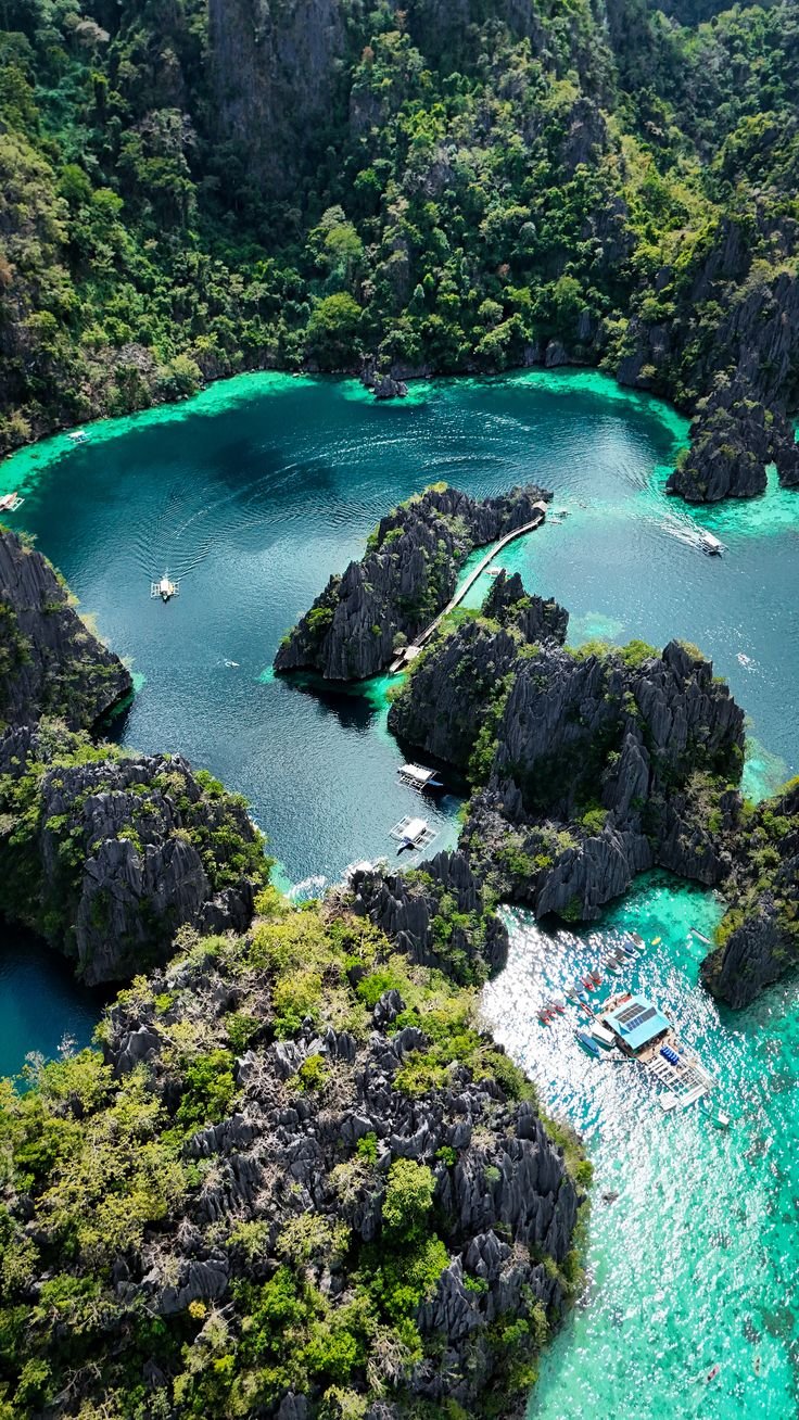 This may contain: an aerial view of boats in the water near some rocks and green trees, surrounded by blue lagoons