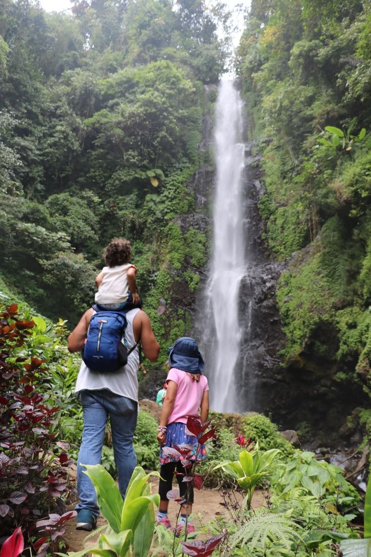 This may contain: two people with backpacks are standing in front of a waterfall