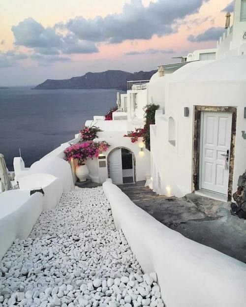 This may contain: a white building with flowers on the roof and water in the background at dusk or dawn