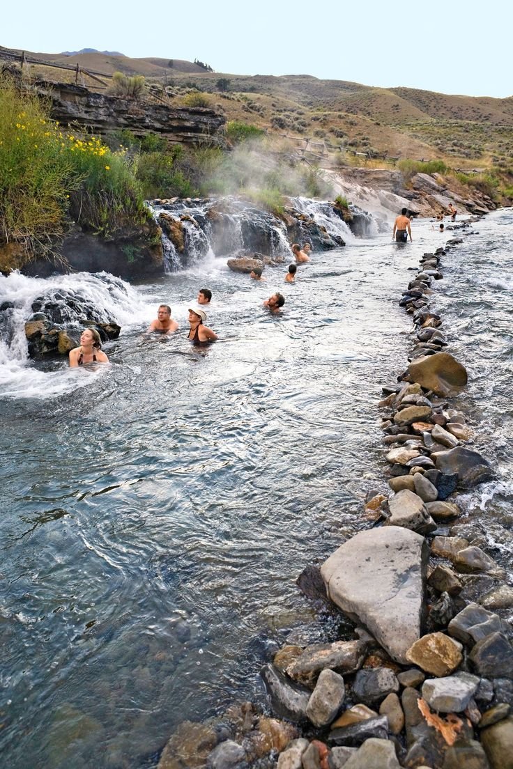 This may contain: several people are swimming in a river with rocks and water cascading around them