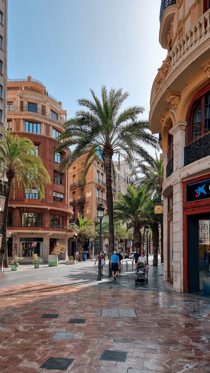 This may contain: people are walking down the street in front of some buildings with palm trees on either side