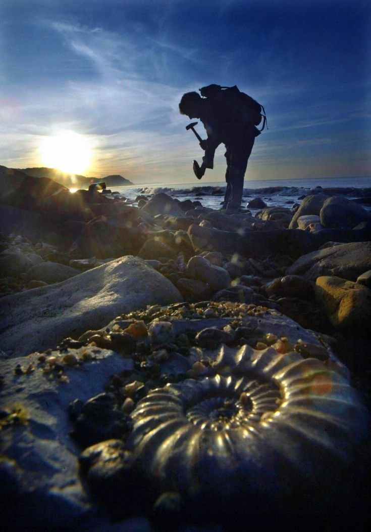 This may contain: a man standing on top of rocks near the ocean